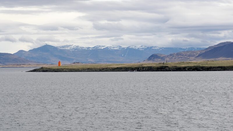 Orange beacon standing on a low grassy island with mountains behind (Engey)