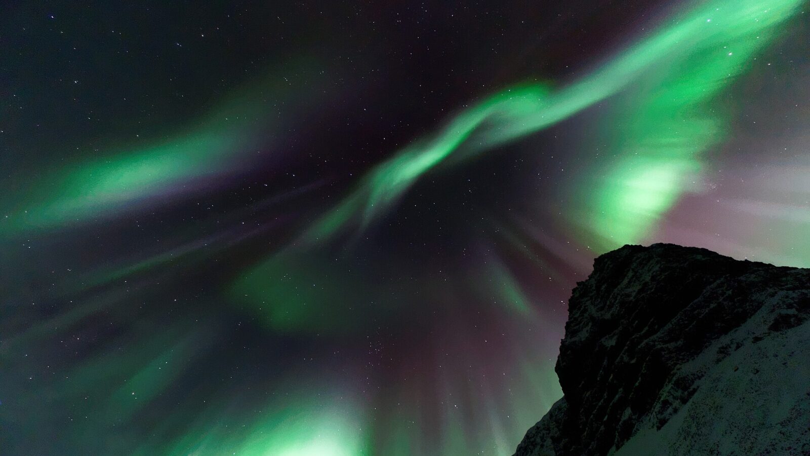 Aurora borealis sweeping across a starry sky above a dark ridge (Vestfirðir)