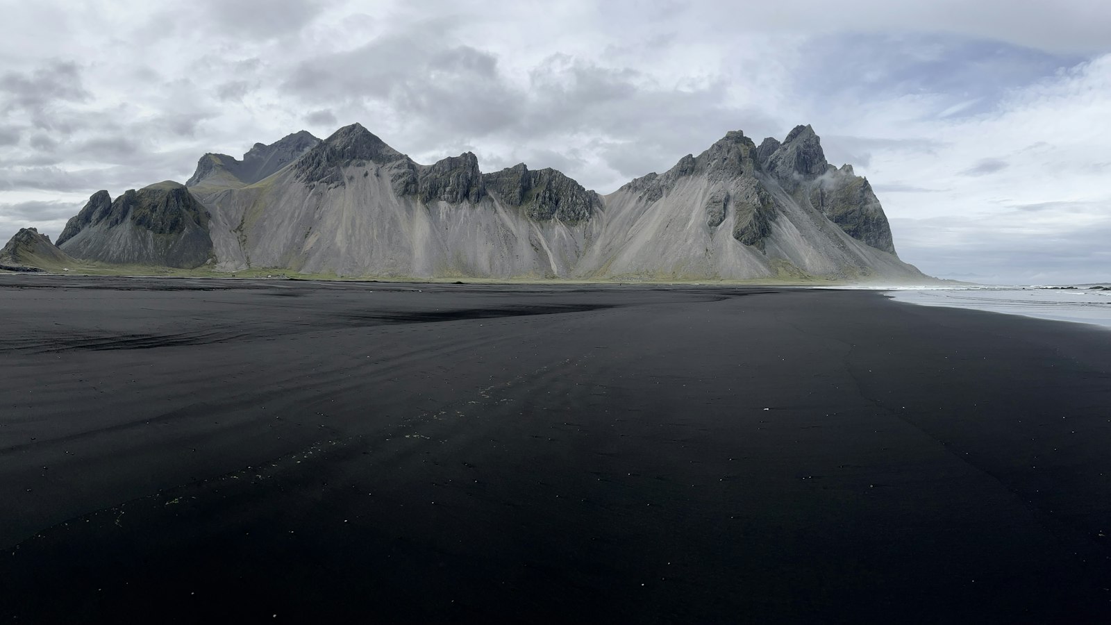 Wide black-sand beach with dramatic mountains on the skyline