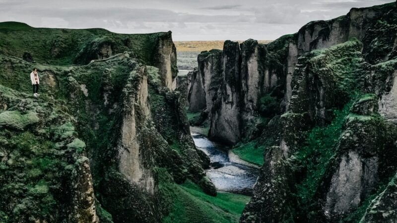 Narrow river cutting through steep, moss-covered canyon with a lone person