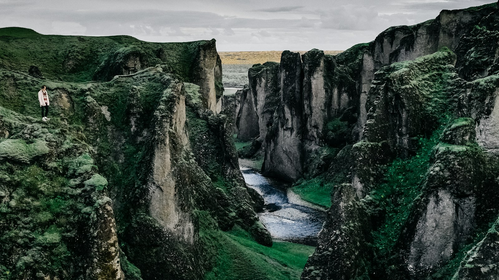 Narrow river cutting through steep, moss-covered canyon with a lone person