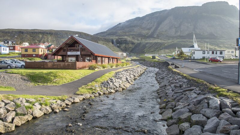 A small river with rock-lined banks and a timber building by the quay (Ólafsvík)