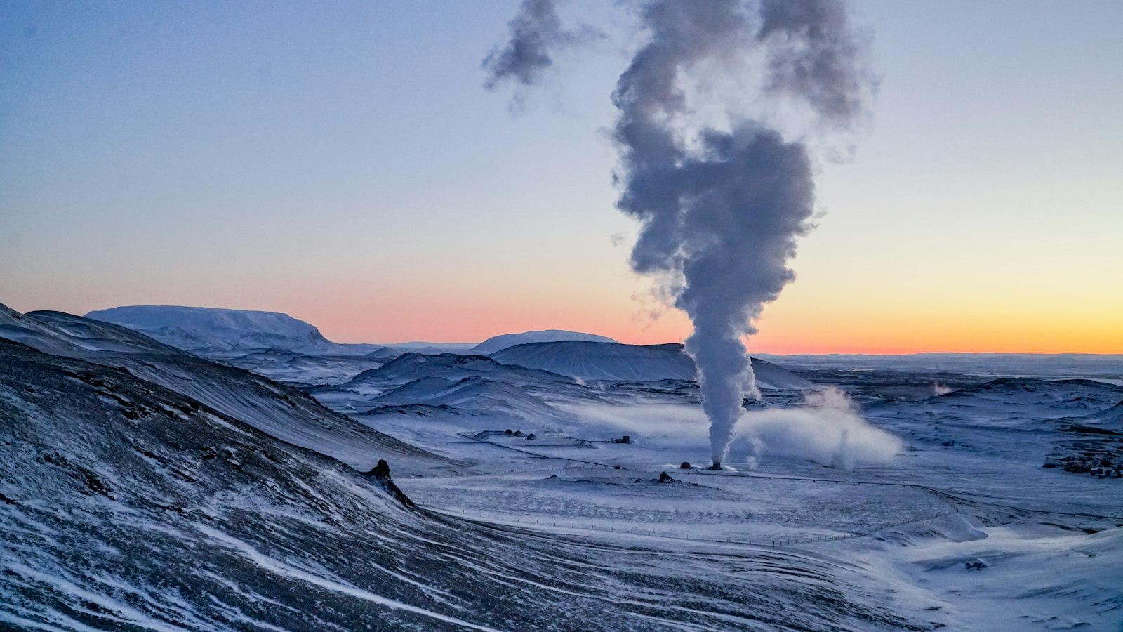 Steam plume rising from a geothermal site in a snowy valley