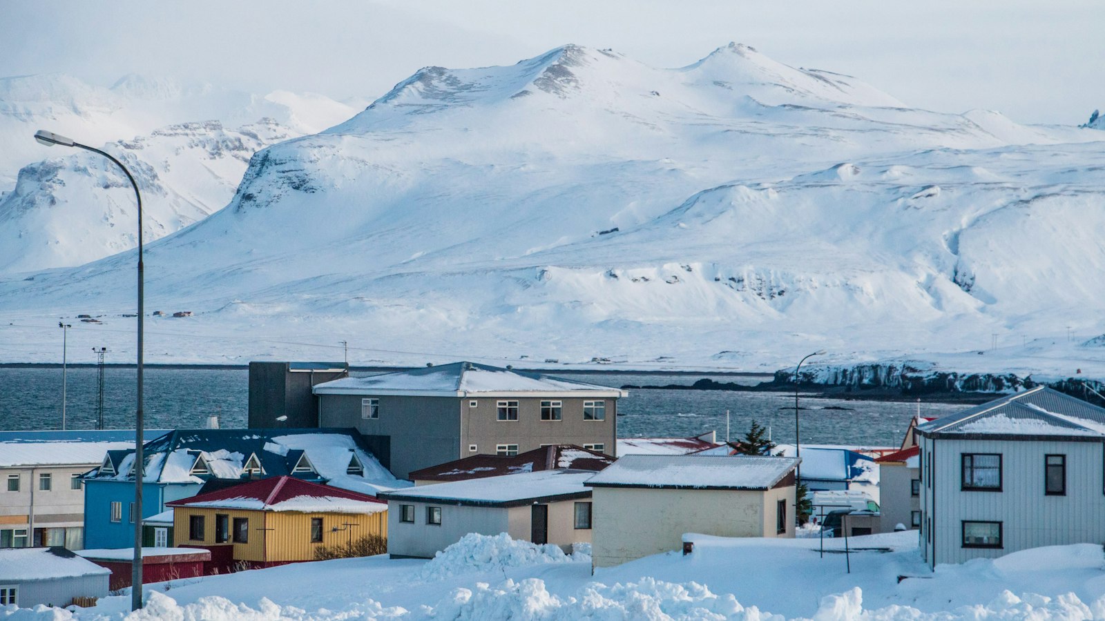 Snowy town rooftops with mountains and sea in background