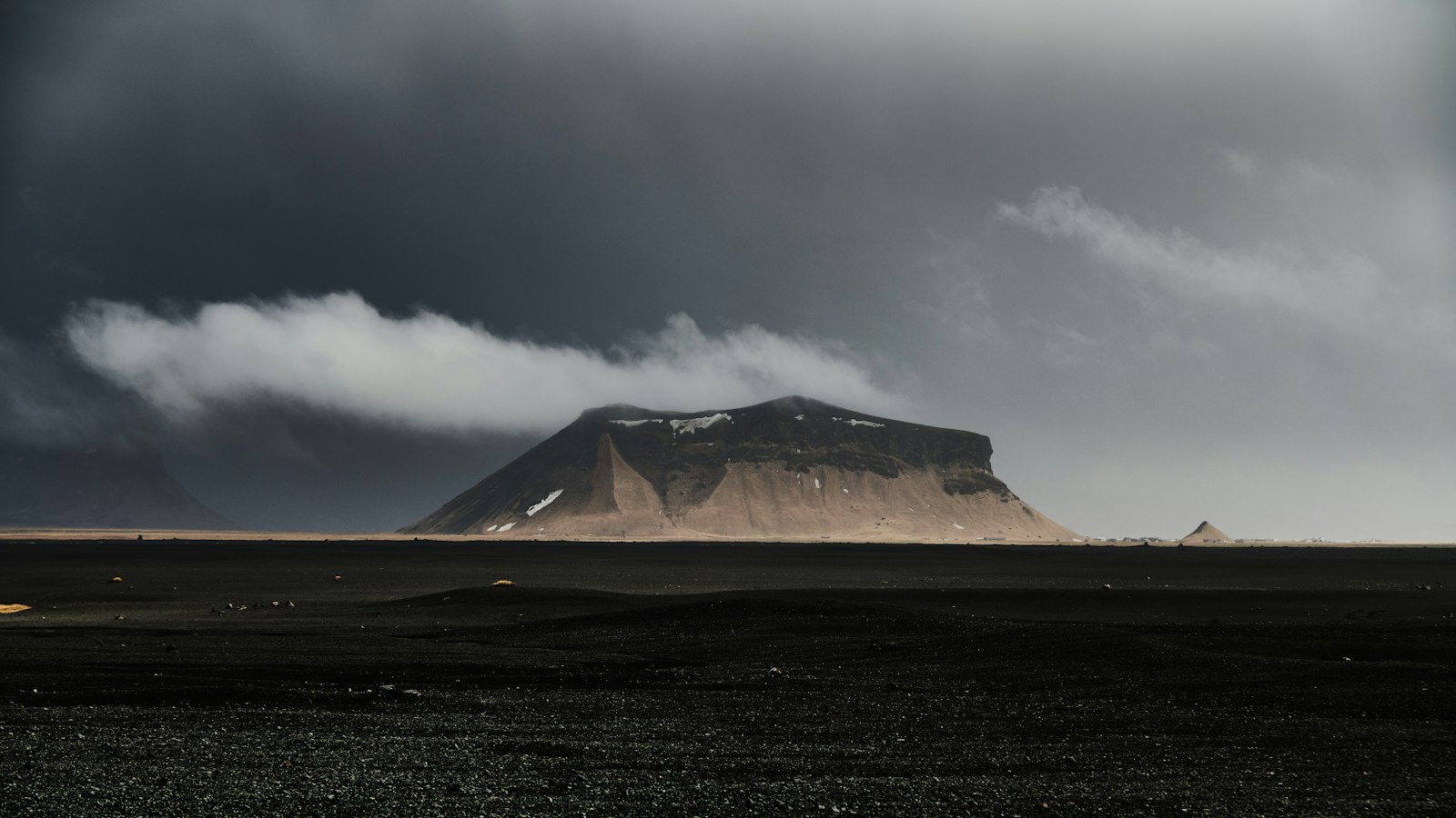 Flat black plain and isolated mountain under heavy clouds
