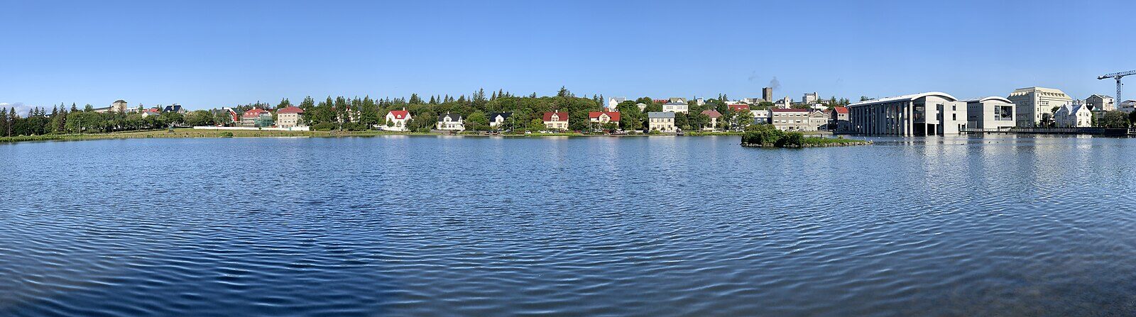 Panoramic view across the lake to city buildings and a modern waterfront hall (Reykjavík)