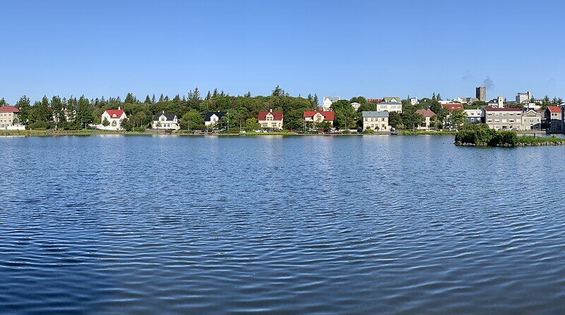 Panoramic view across the lake to city buildings and a modern waterfront hall (Reykjavík)