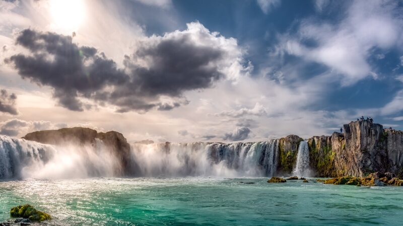 Panoramic view of waterfall with cliffs and visitors on the rim (Goðafoss)