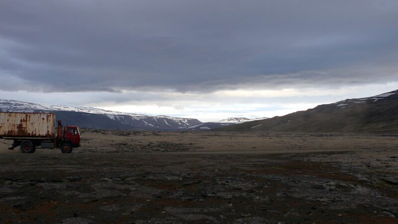 Truck on a gravel plain beneath a cloudy sky (Surtshellir)