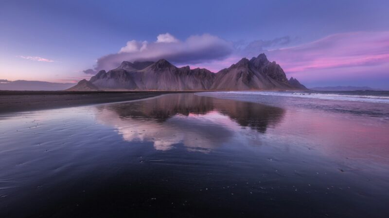 Vestrahorn mountain reflected in wet black sand
