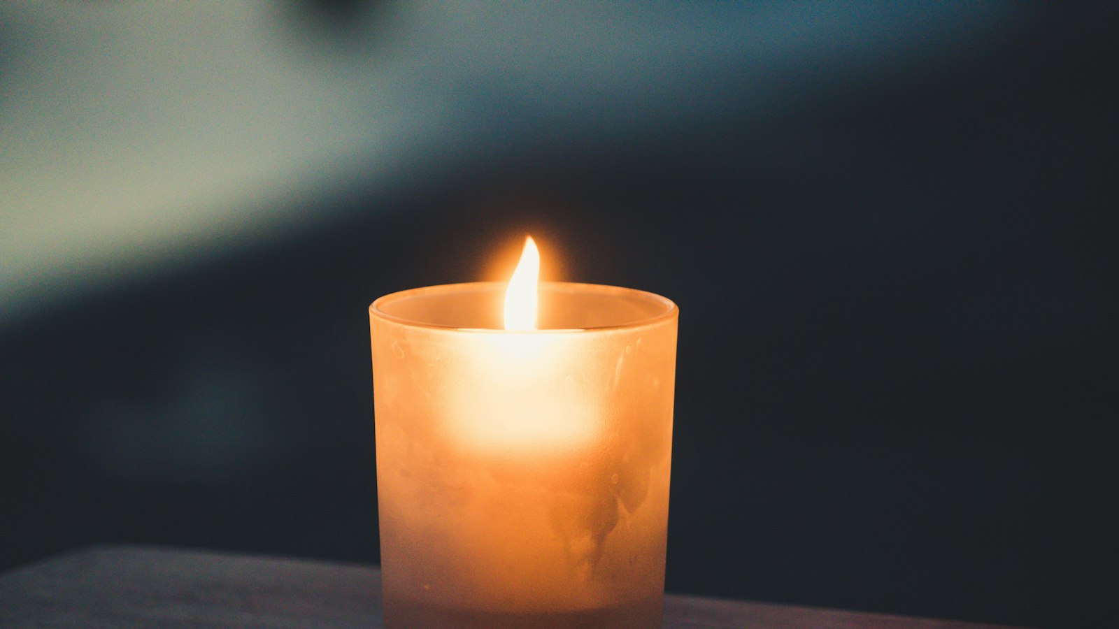 A lit candle in a frosted glass holder