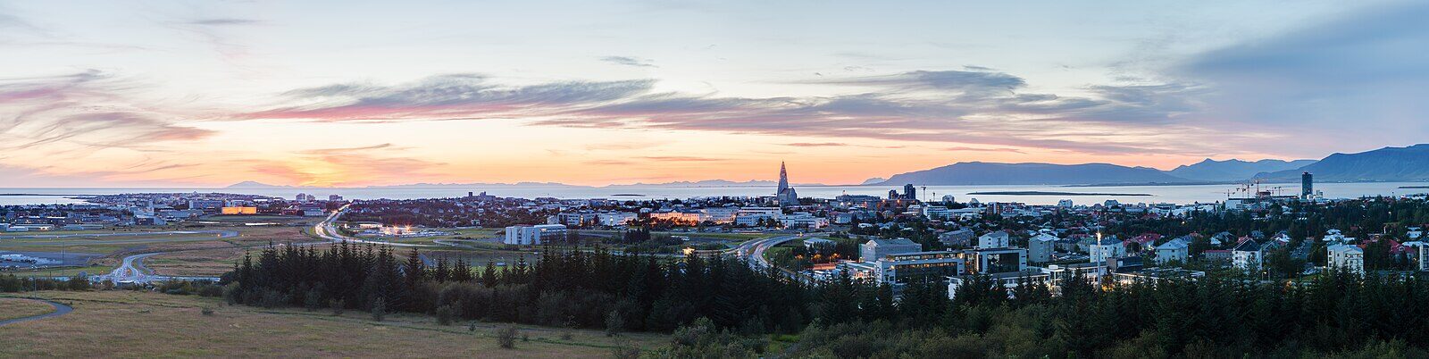 Panoramic cityscape with distant church spire and coastal horizon at sunset (Reykjavík)