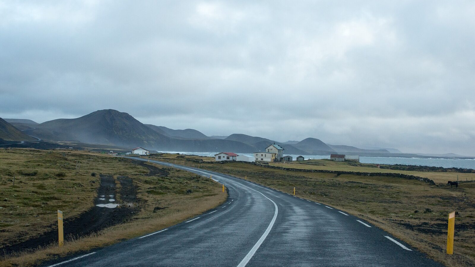 Coastal road curving towards low volcanic hills and houses (Grindavík)