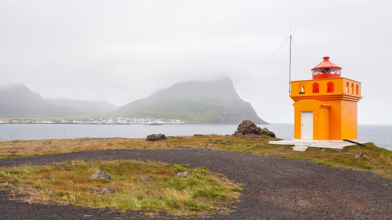 Small orange lighthouse on a rocky headland beside the sea (Westfjords)