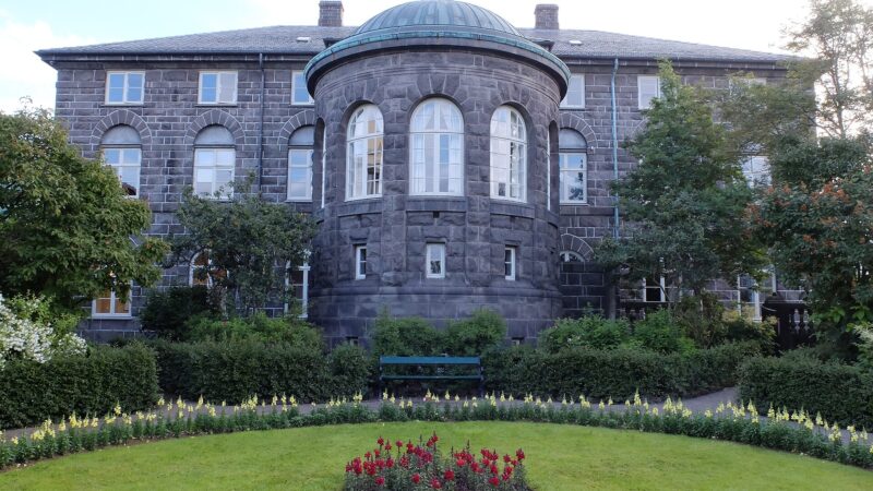 Stone building facade with rounded projection and flowerbed in front (Alþingi)
