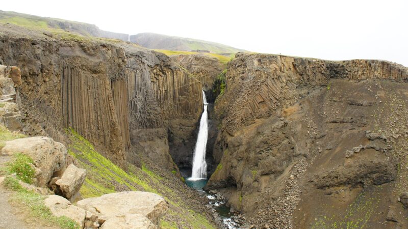 Waterfall dropping between steep basalt columns in a rocky gorge (Hjálpleysa)