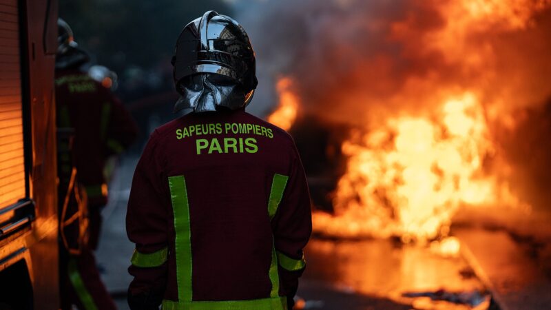 Firefighter in turnout gear facing a large street blaze (Paris)