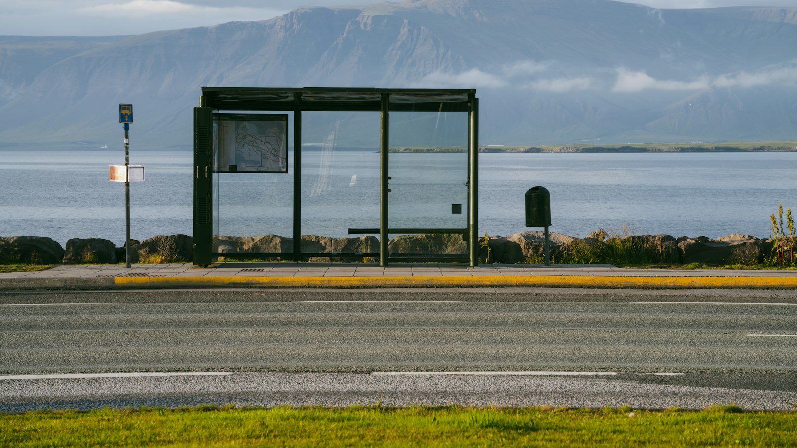 Empty glass bus shelter with sea and mountains in the background