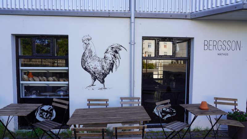 Outdoor tables and a rooster mural on a cafe wall (Alþingi)