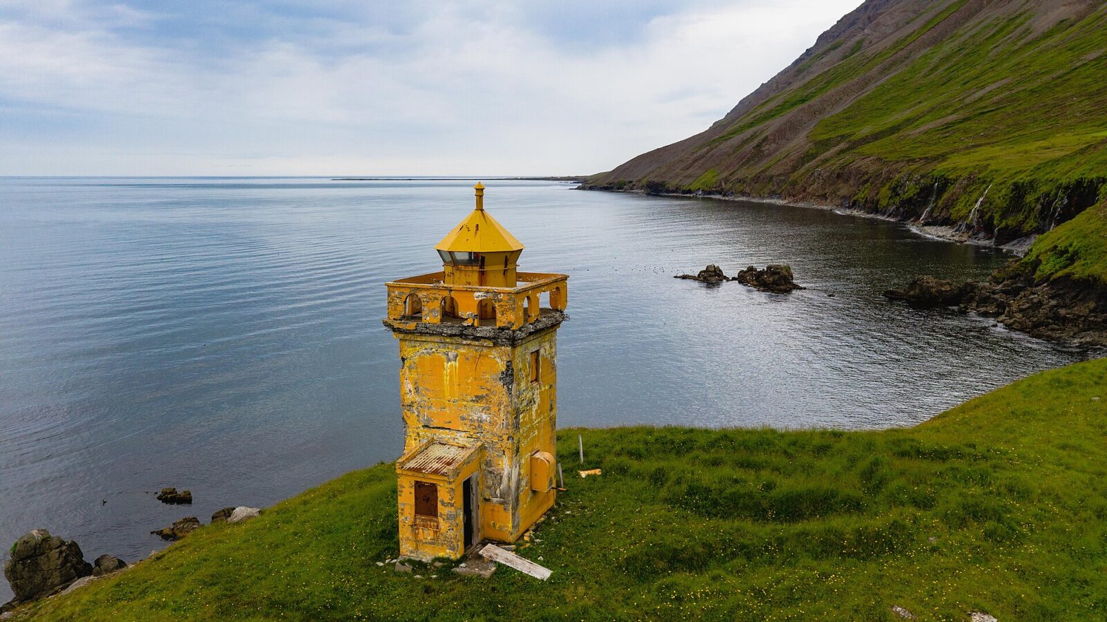 Yellow lighthouse tower by a calm bay and steep cliffs (Norðurland vestra)