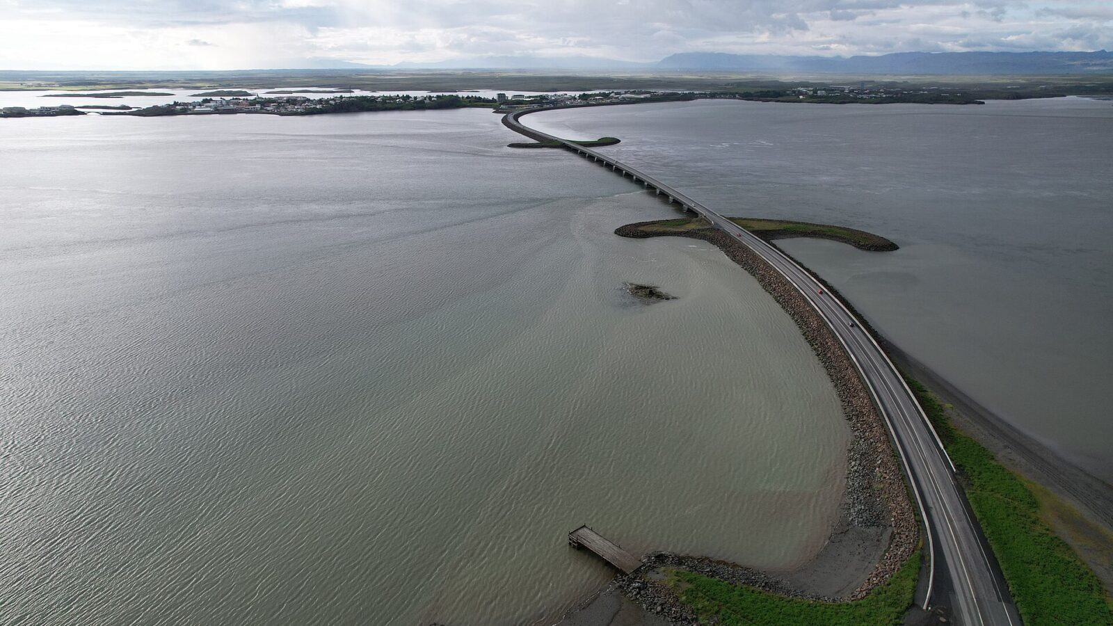 Long coastal causeway stretching toward a town and mountains. (Borgarnes)