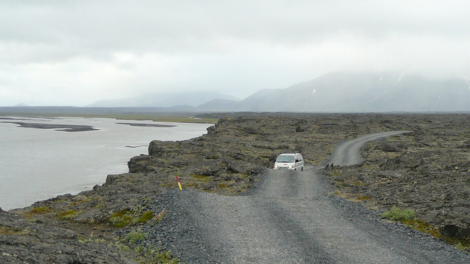 Gravel track along a rocky shoreline with a vehicle on the road
