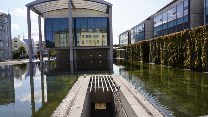 A modern concrete-and-glass building reflected in a shallow pool (University of Iceland (Háskóli Íslands))