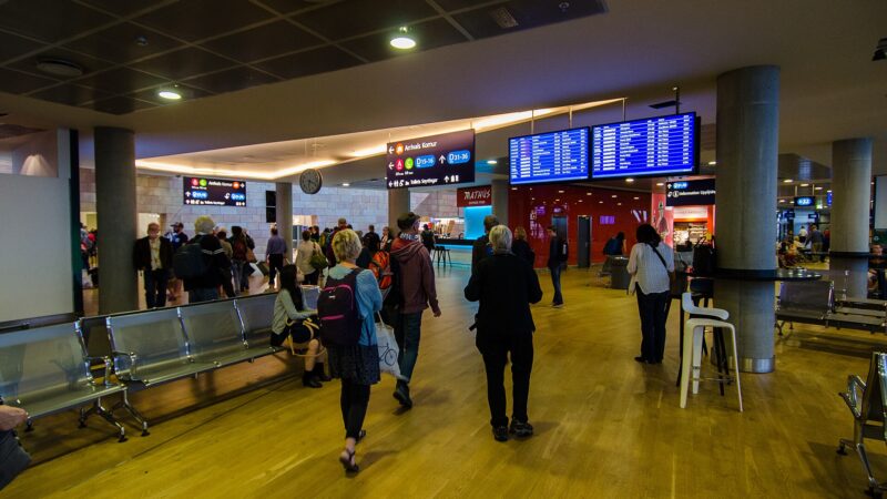 Passengers walk through an airport departure area under information screens (Keflavík)