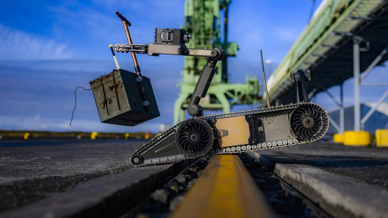 Explosive‑ordnance robot holding a suspicious object at a dock (Straumsvík)