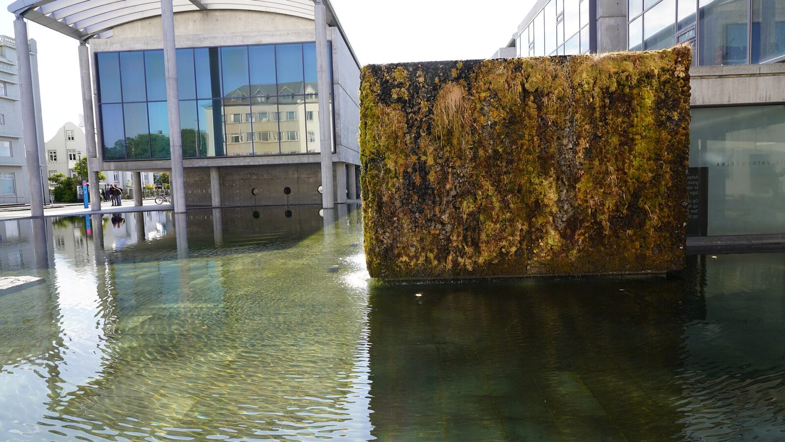 A moss-covered rectangular fountain block by shallow water (Reykjavík)