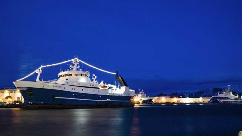 A large trawler moored at a harbour under deep-blue dusk sky