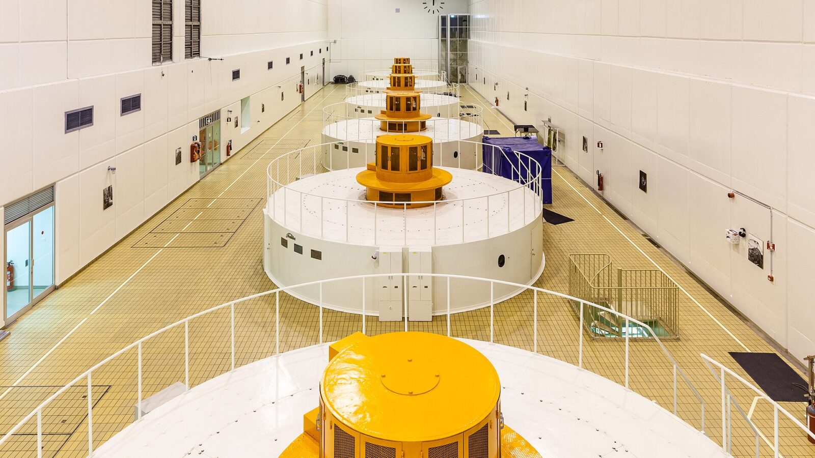 Interior hall with a row of large white generator housings and yellow tops (Landsvirkjun)