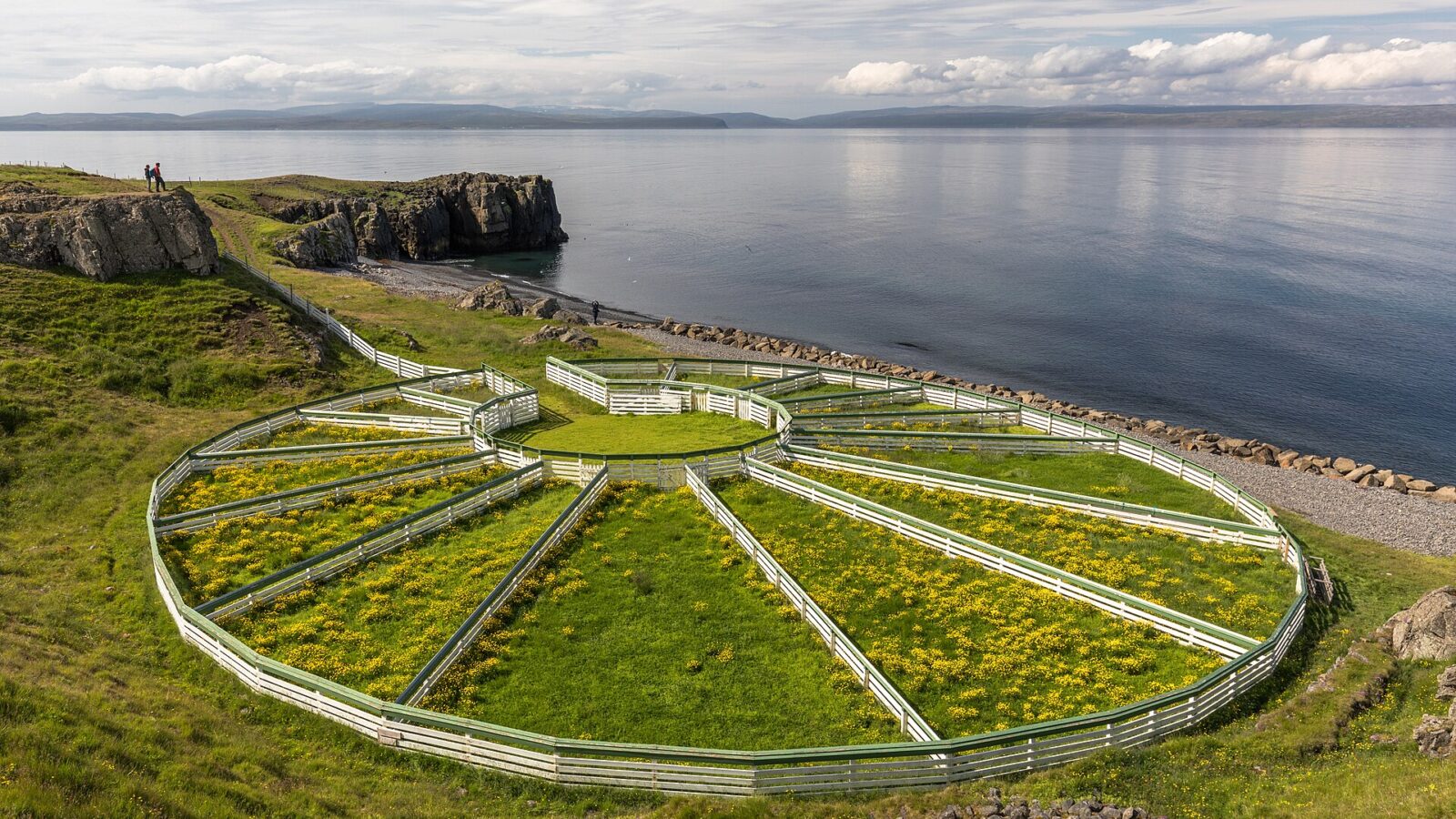 Coastal headland with circular wooden sheepfold and calm fjord (Húnaþing vestra)