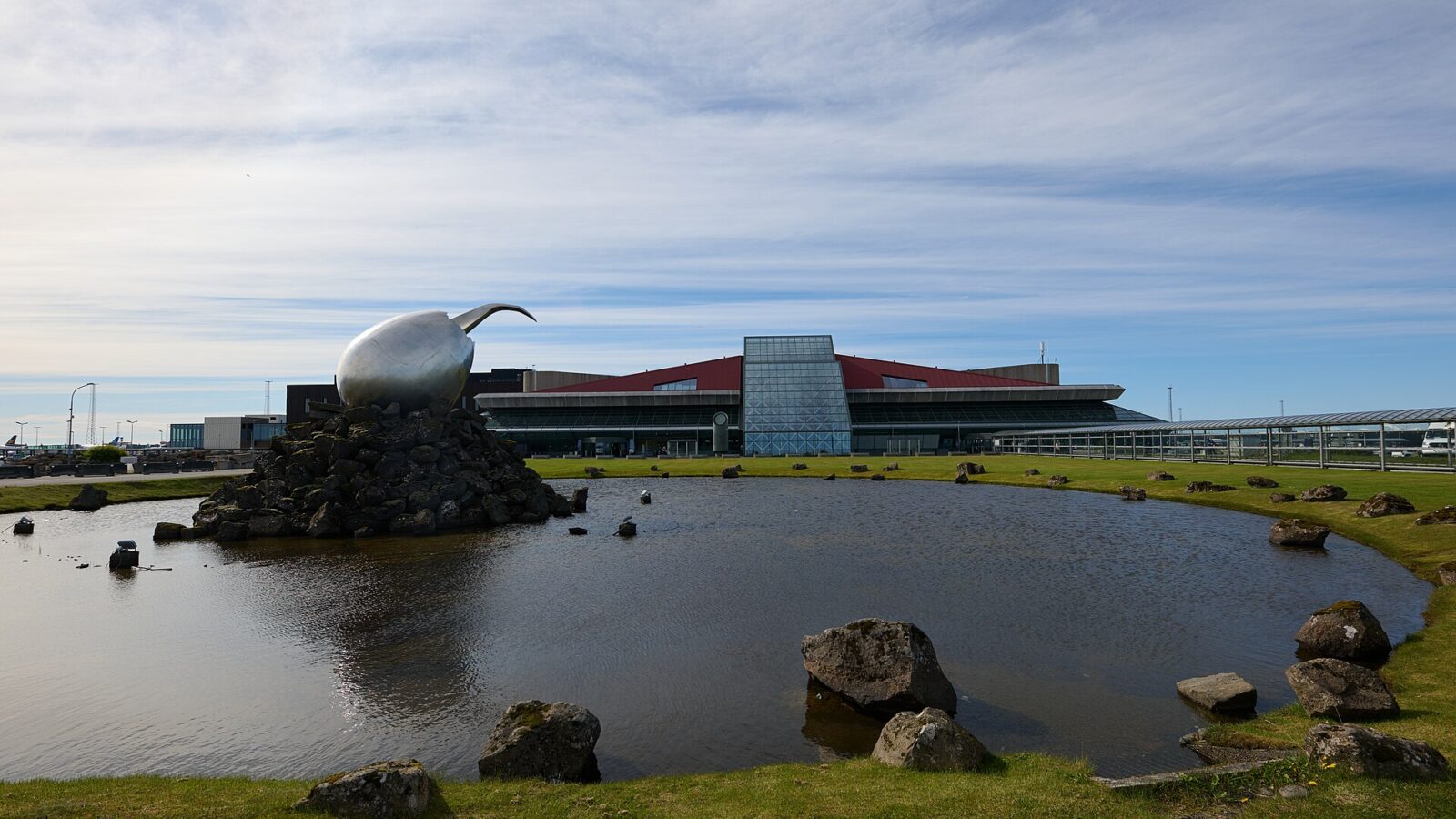 Exterior view of an airport terminal with sculpture and pond (Keflavík Airport)