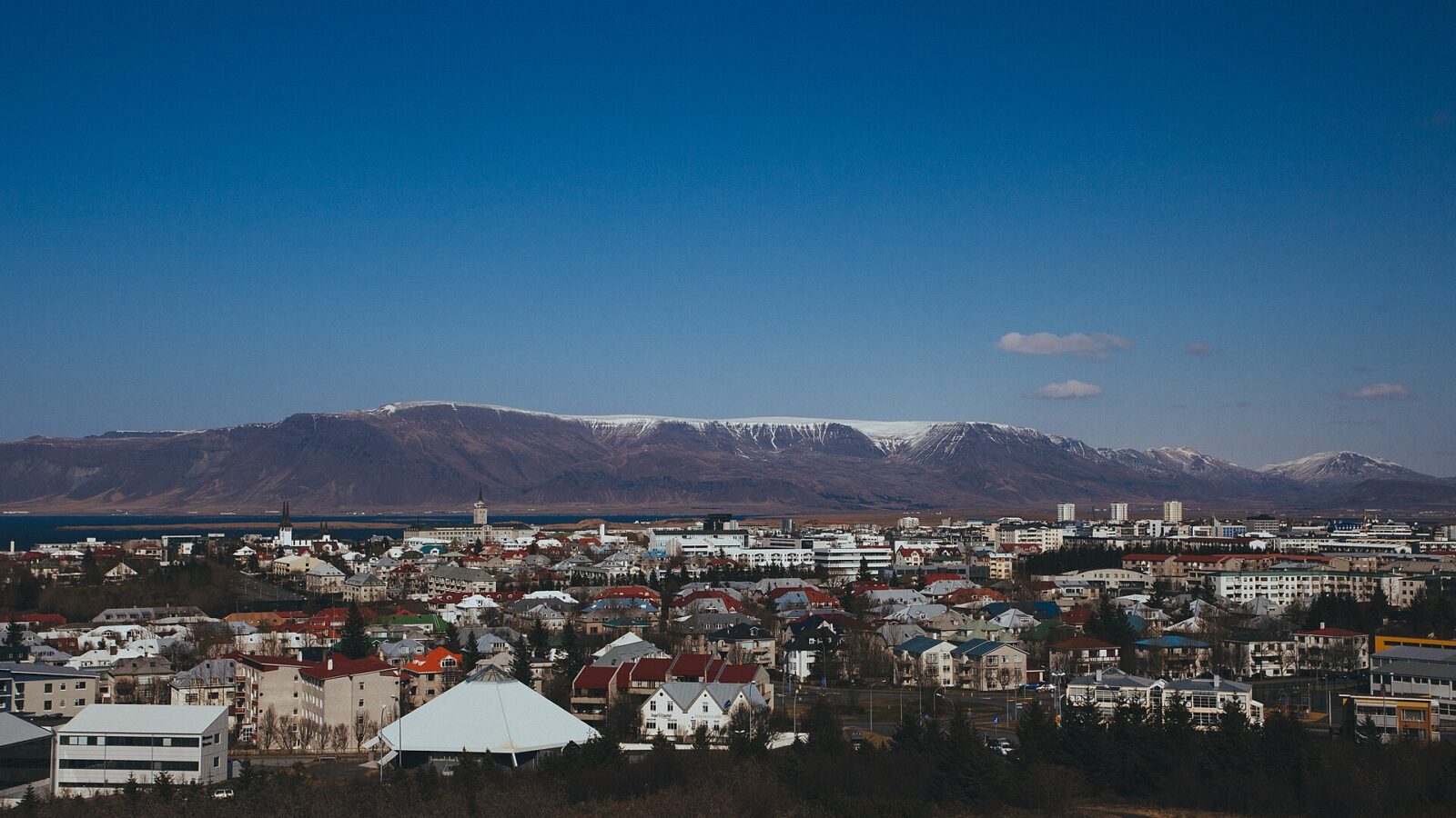 City foreground with mountains and clear blue sky behind (Mosfellsheiði)