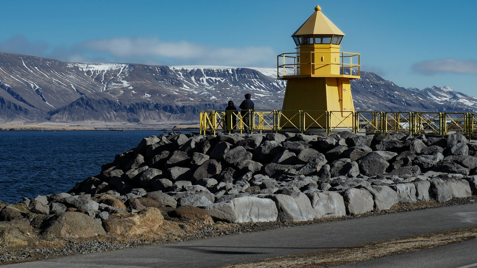 Yellow lighthouse on rocky breakwater with two people nearby