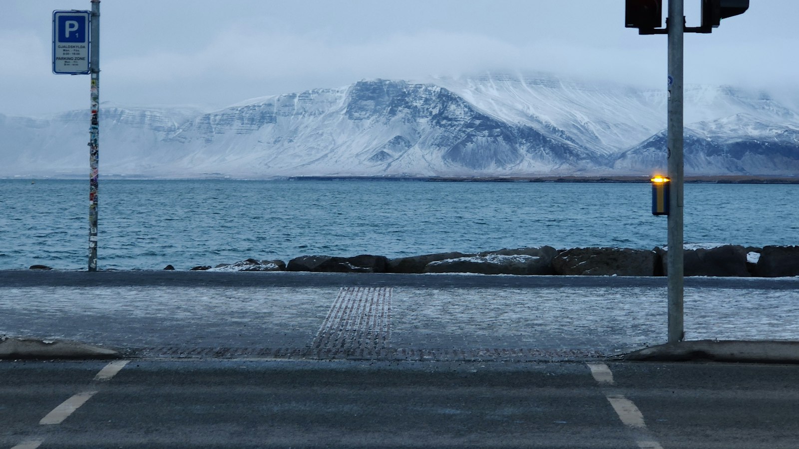 Coastal street with sea and snow-covered mountain in the background