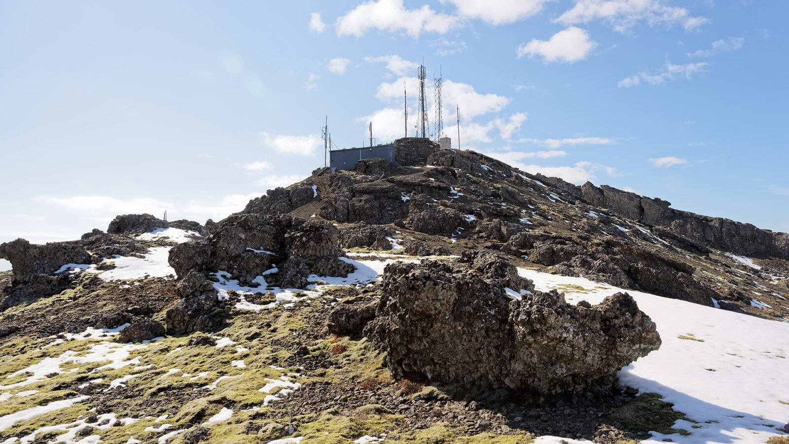 Rocky hill with communications masts and patches of snow (Grindavík)