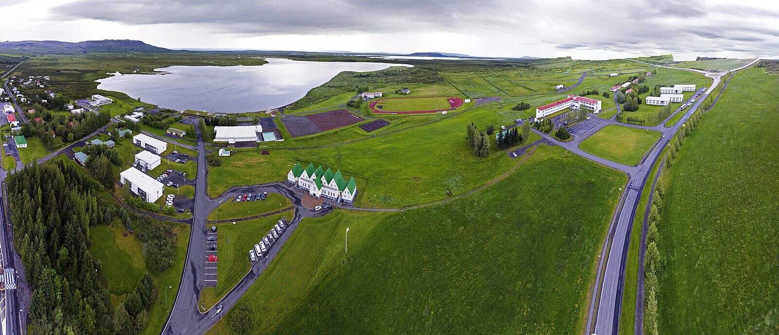 Aerial view of a lakeside village with buildings, roads and parked cars (Laugarvatn)