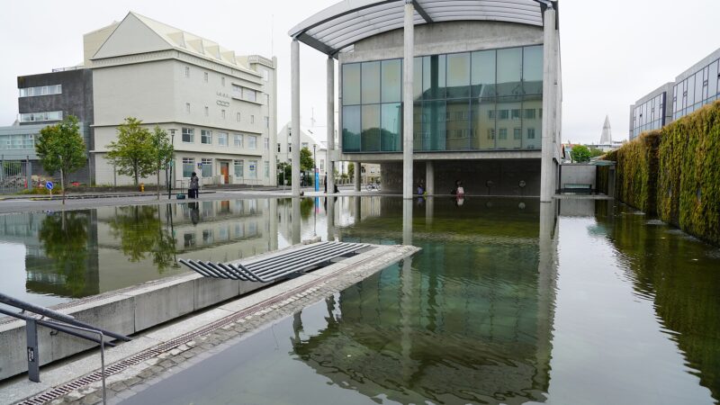 Office building and reflecting pool with moss-covered wall at right (Reykjavík)