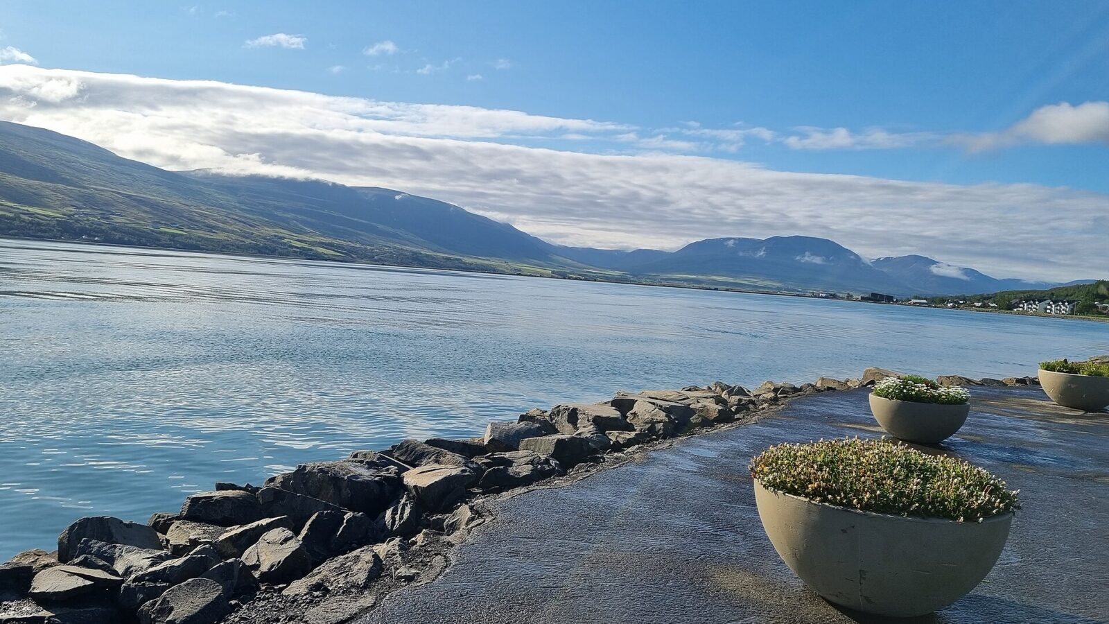 Rocky shore and waterfront path with distant town (Akureyri)