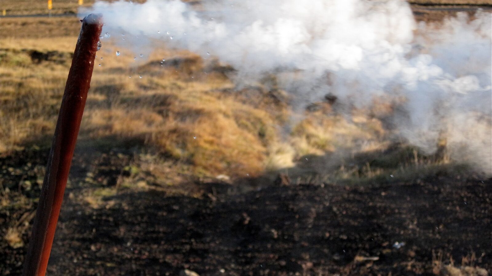 Steam venting from a rusty pipe over grassy ground