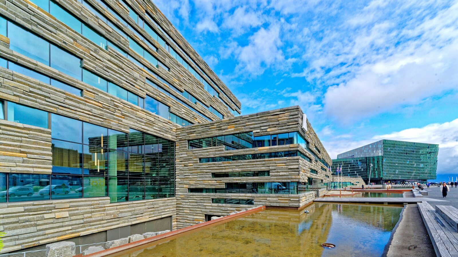 Exterior of a stone‑clad building beside a reflecting pool (Harpa)