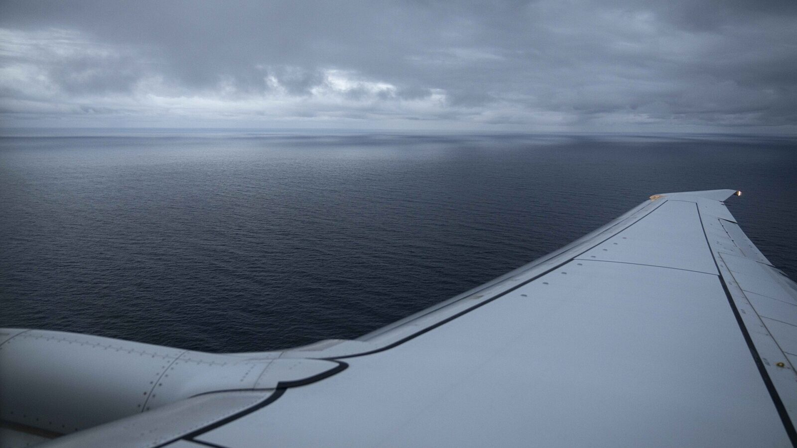 Airliner wing above the sea beneath a cloudy sky