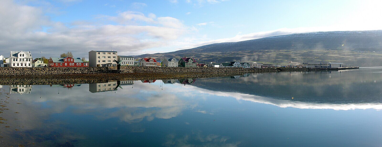 Harbour front and row of coastal buildings reflected in calm water (Akureyri)