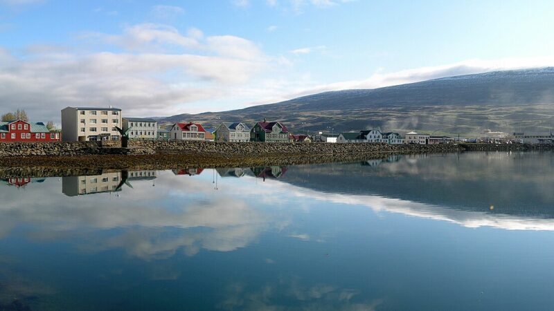 Harbour front and row of coastal buildings reflected in calm water (Akureyri)