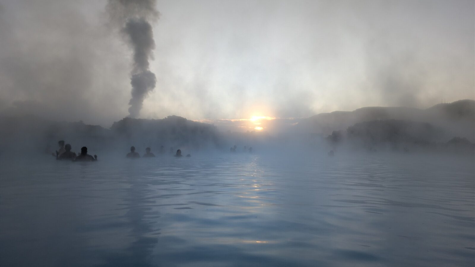 Steam rising above a lagoon with silhouetted bathers and sun (Blue Lagoon)