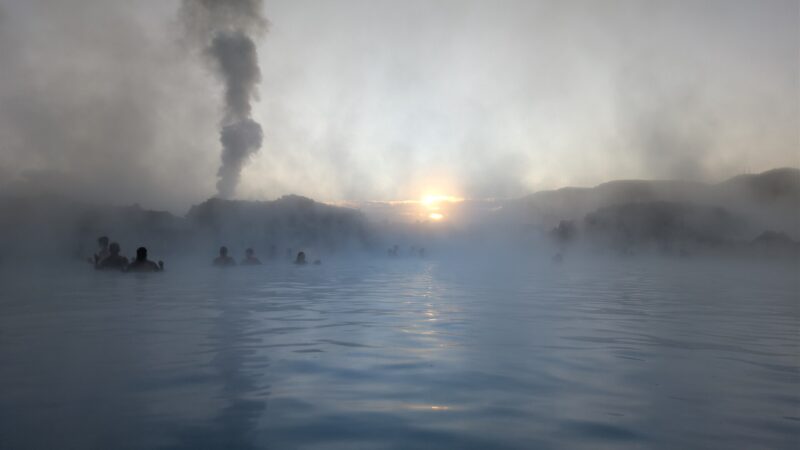 Steam rising above a lagoon with silhouetted bathers and sun (Blue Lagoon)