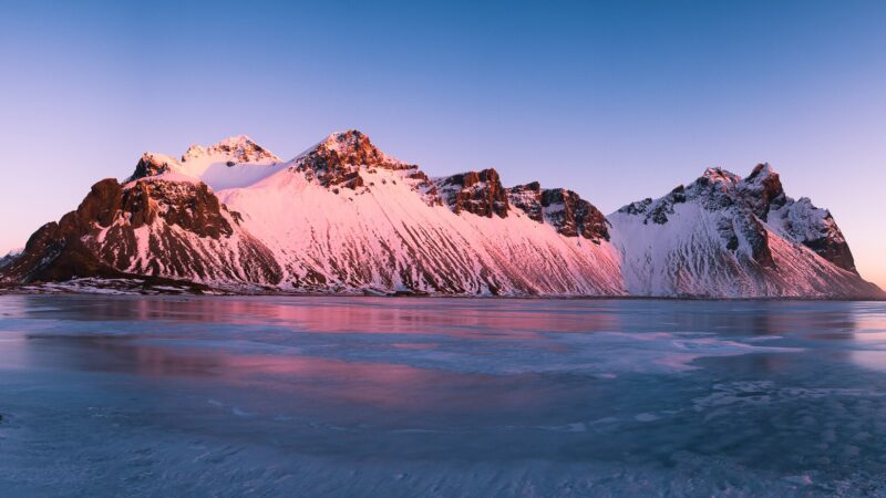 Snow-capped rugged mountains glowing pink at dawn