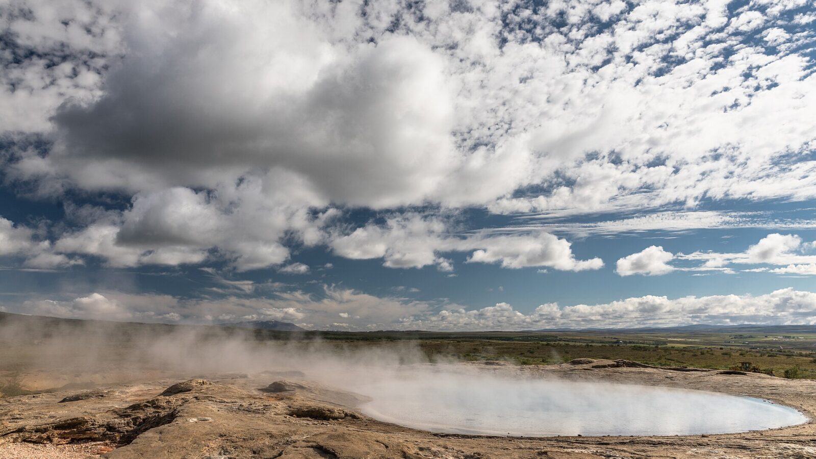 Geothermal pool rim with steam and broad cloudy sky (Great Geysir)